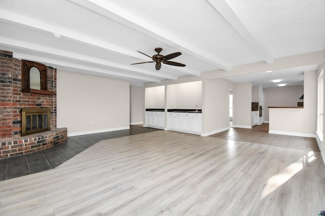 unfurnished living room with a fireplace, ceiling fan, hardwood / wood-style floors, and beamed ceiling