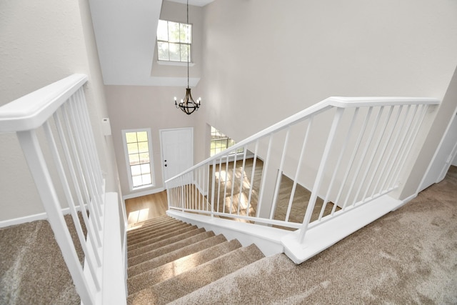 staircase featuring a notable chandelier, a healthy amount of sunlight, carpet floors, and a towering ceiling