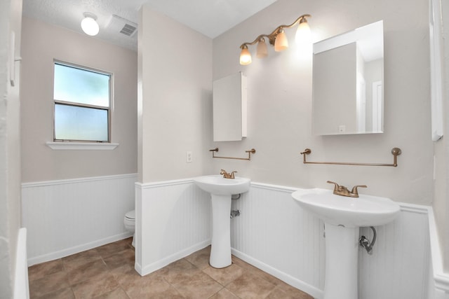 bathroom featuring tile patterned floors, toilet, and double sink