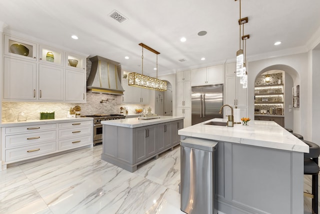 kitchen featuring custom exhaust hood, a large island with sink, sink, decorative light fixtures, and premium appliances