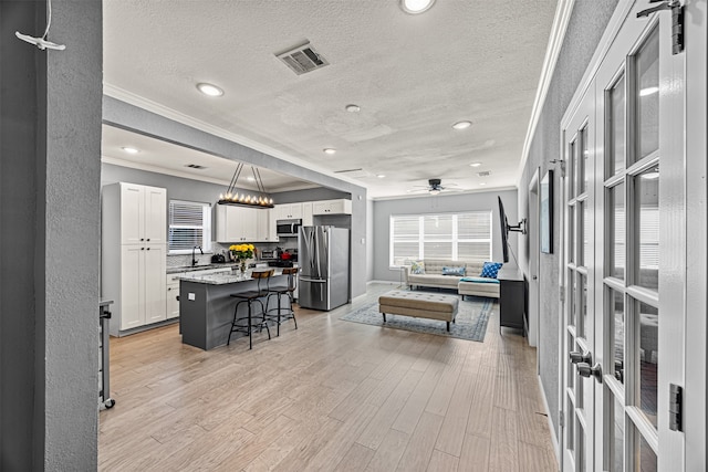 interior space with light wood-type flooring, ceiling fan with notable chandelier, a textured ceiling, crown molding, and sink