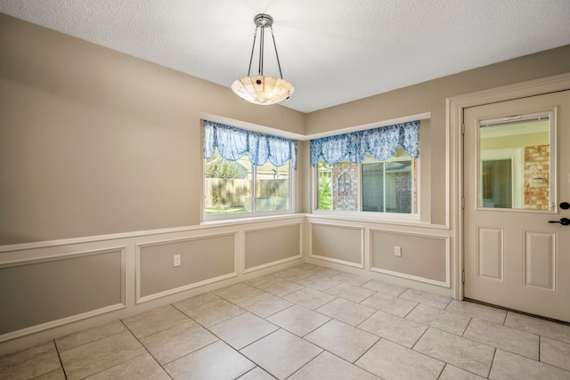 unfurnished dining area with light tile patterned floors, a chandelier, and a textured ceiling