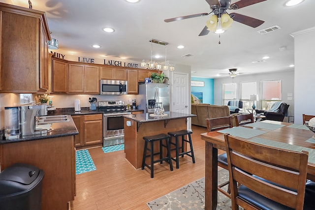 kitchen featuring ceiling fan, a center island, stainless steel appliances, light hardwood / wood-style flooring, and decorative light fixtures