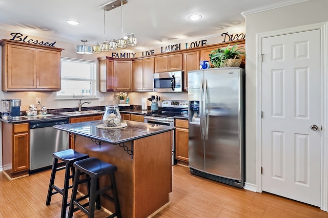 kitchen with a center island, sink, light wood-type flooring, appliances with stainless steel finishes, and decorative light fixtures