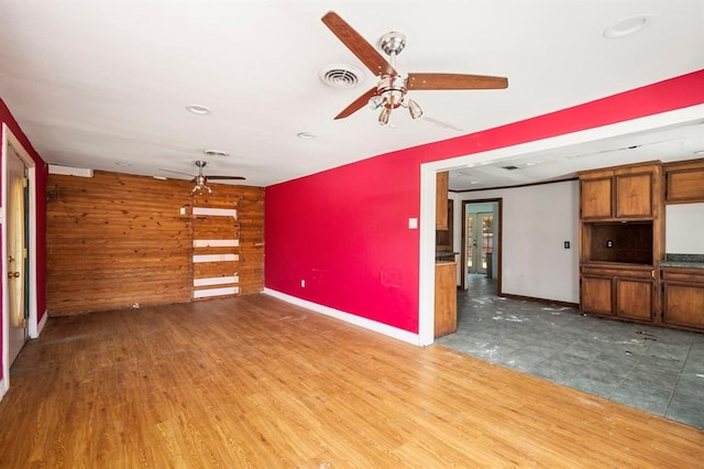 unfurnished living room with wood walls, hardwood / wood-style floors, and ceiling fan