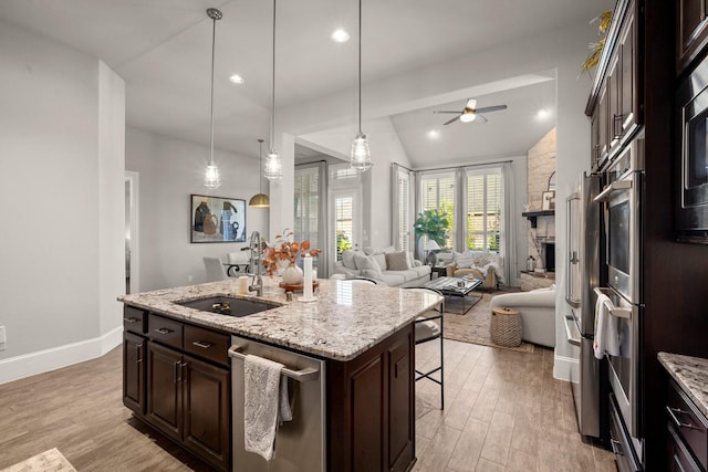 kitchen with sink, dark brown cabinets, light stone counters, a center island with sink, and decorative light fixtures