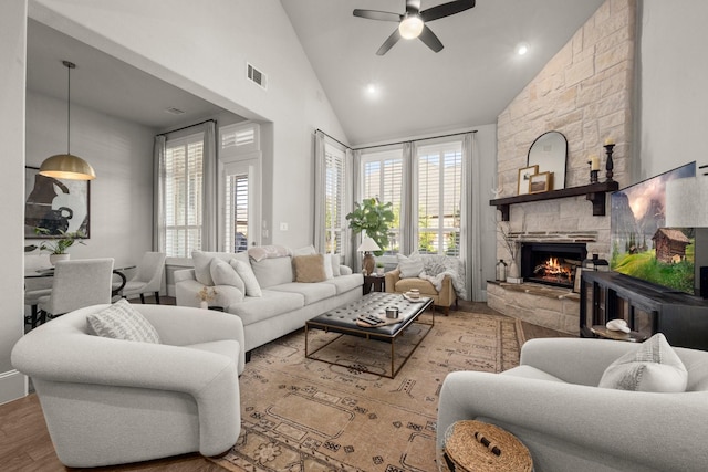 living room with ceiling fan, wood-type flooring, a stone fireplace, and high vaulted ceiling