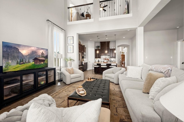 living room with dark wood-type flooring, ceiling fan, and a high ceiling