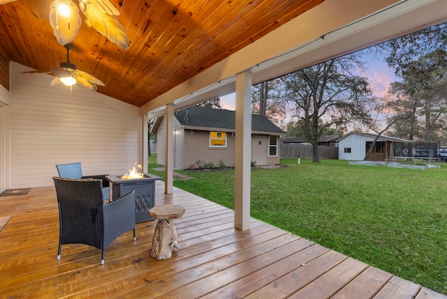 deck at dusk with a fire pit, an outbuilding, and a yard