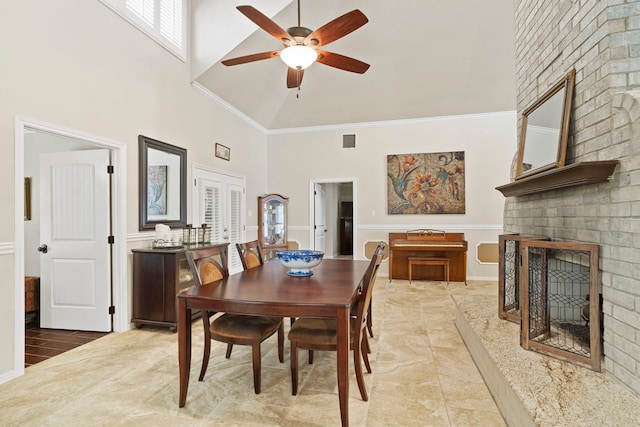 dining space with a brick fireplace, ceiling fan, crown molding, high vaulted ceiling, and light tile patterned flooring