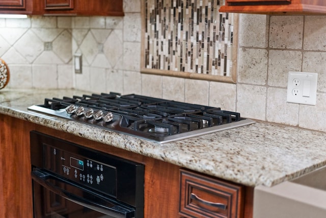 kitchen featuring black oven, decorative backsplash, light stone countertops, and stainless steel gas cooktop