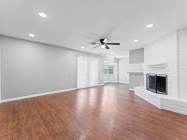 unfurnished living room featuring ceiling fan, dark wood-type flooring, and a brick fireplace