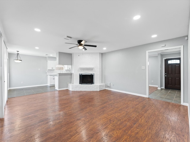 unfurnished living room featuring a fireplace, dark hardwood / wood-style flooring, and ceiling fan