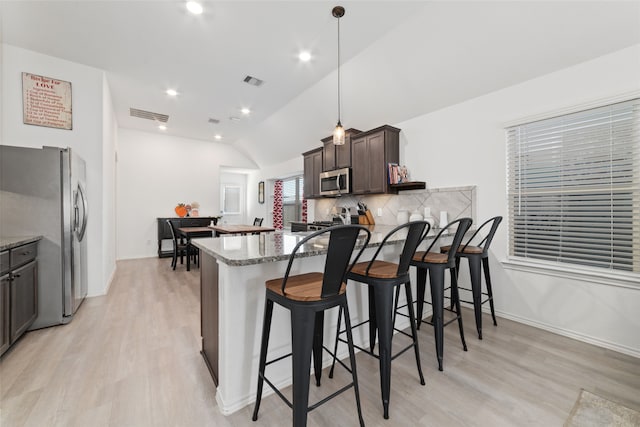 kitchen featuring stainless steel appliances, a kitchen breakfast bar, dark stone counters, lofted ceiling, and dark brown cabinets