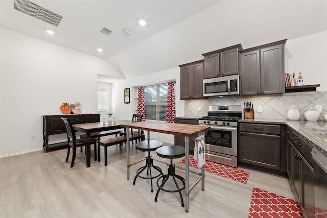 kitchen featuring light stone countertops, light hardwood / wood-style floors, vaulted ceiling, dark brown cabinets, and appliances with stainless steel finishes