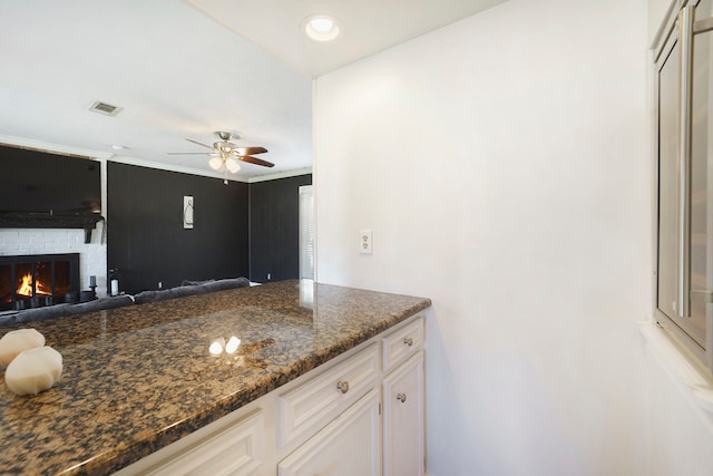 kitchen featuring ceiling fan, a fireplace, white cabinets, and dark stone counters