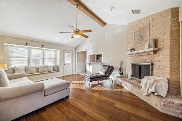 living room with a brick fireplace, a textured ceiling, ceiling fan, hardwood / wood-style floors, and vaulted ceiling with beams