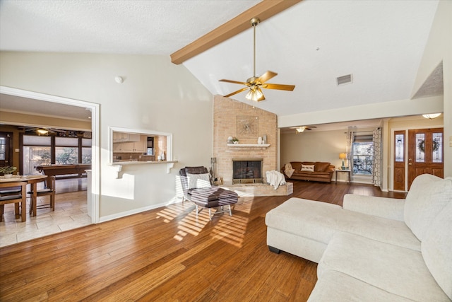 living room featuring beam ceiling, ceiling fan, a large fireplace, high vaulted ceiling, and light hardwood / wood-style floors