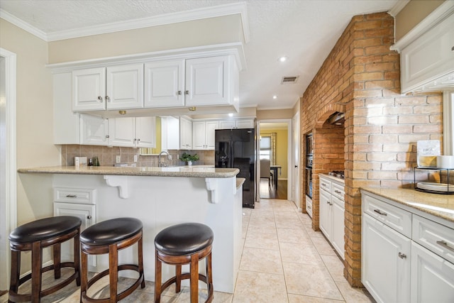 kitchen featuring a kitchen bar, light stone countertops, black refrigerator, tasteful backsplash, and white cabinetry