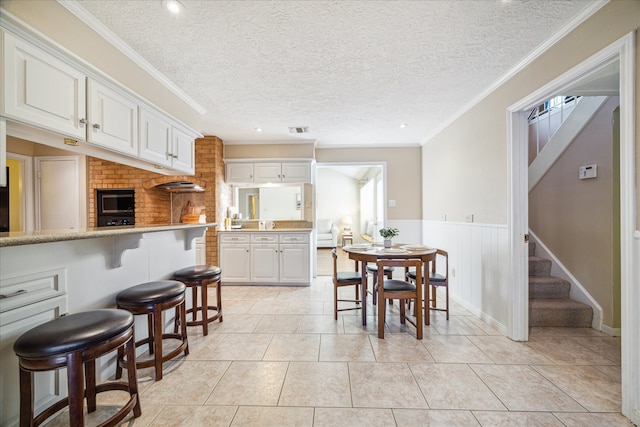 kitchen with a textured ceiling, a breakfast bar, white cabinetry, and crown molding