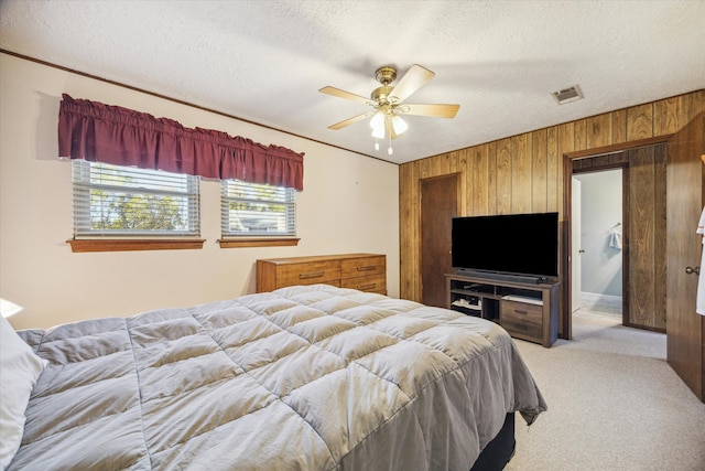 bedroom with wooden walls, ceiling fan, light colored carpet, and a textured ceiling