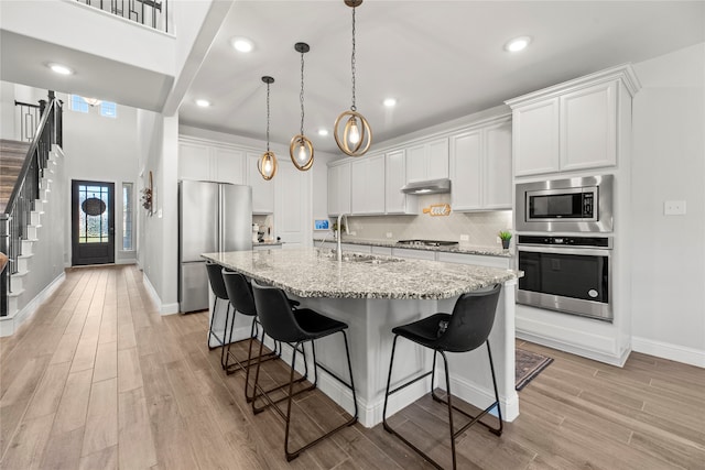 kitchen featuring appliances with stainless steel finishes, a kitchen island with sink, sink, light hardwood / wood-style flooring, and white cabinets