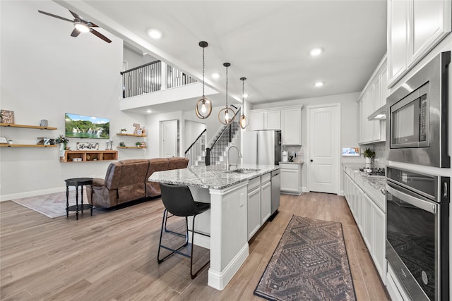 kitchen featuring a center island with sink, white cabinets, light hardwood / wood-style flooring, light stone countertops, and stainless steel appliances