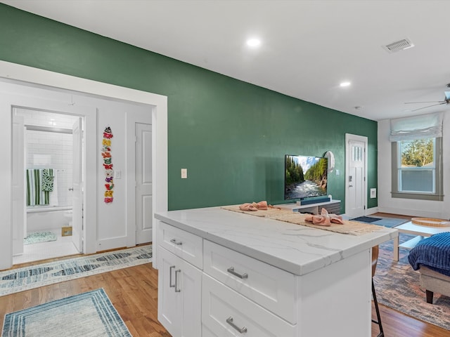 kitchen featuring light stone countertops, a kitchen island, light hardwood / wood-style flooring, white cabinetry, and a breakfast bar area