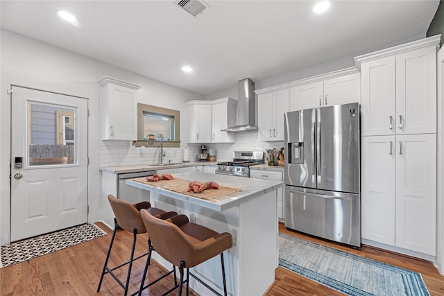 kitchen featuring appliances with stainless steel finishes, light wood-type flooring, wall chimney exhaust hood, white cabinetry, and a breakfast bar area