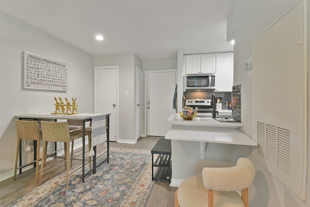 kitchen featuring backsplash, white cabinets, light hardwood / wood-style floors, kitchen peninsula, and stainless steel appliances