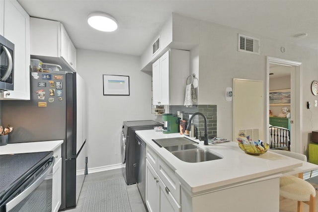 kitchen with white cabinetry, sink, a kitchen breakfast bar, washer and clothes dryer, and appliances with stainless steel finishes