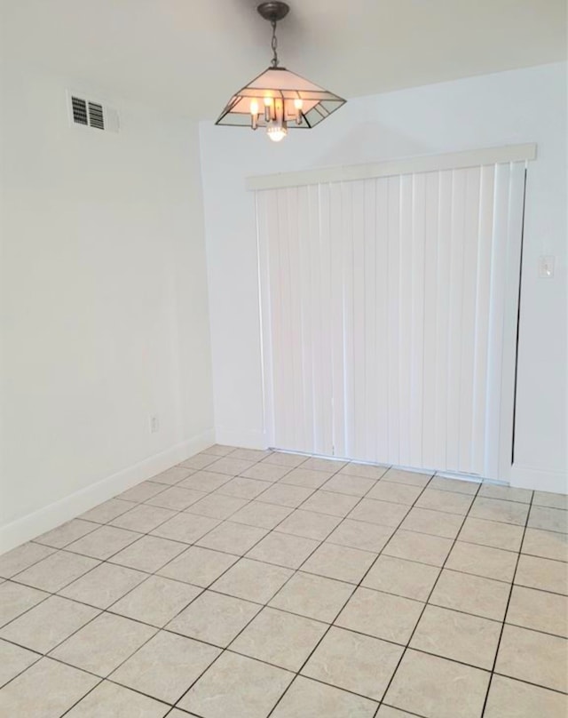 tiled spare room featuring an inviting chandelier