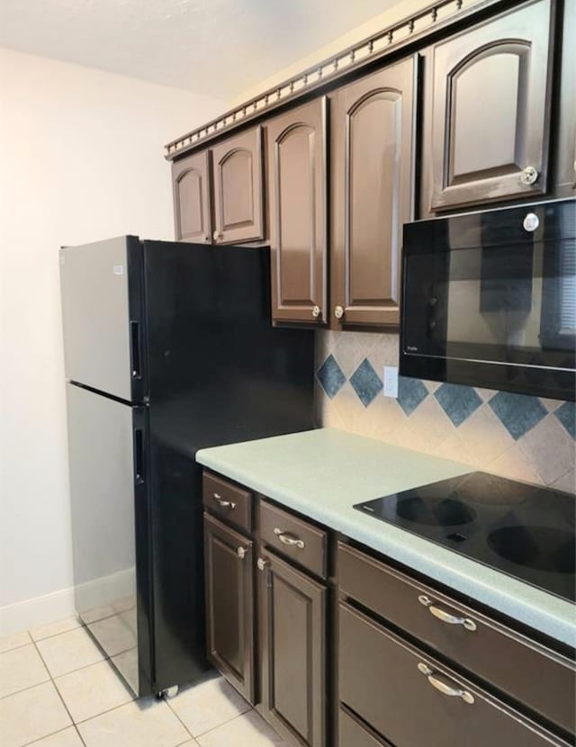 kitchen featuring black appliances, light tile patterned flooring, dark brown cabinetry, and tasteful backsplash