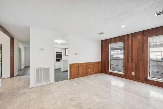 empty room with wood walls, a healthy amount of sunlight, and a textured ceiling