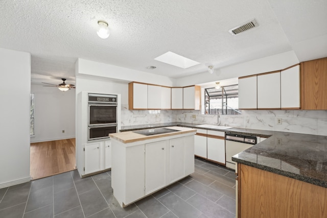 kitchen with black appliances, sink, a skylight, a kitchen island, and white cabinetry