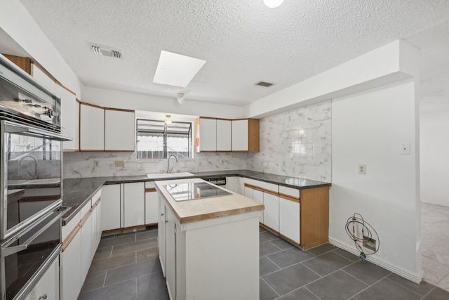 kitchen featuring a skylight, a textured ceiling, a kitchen island, sink, and white cabinetry