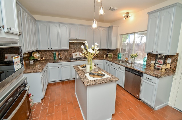 kitchen with a kitchen island, sink, dark stone counters, hanging light fixtures, and stainless steel appliances