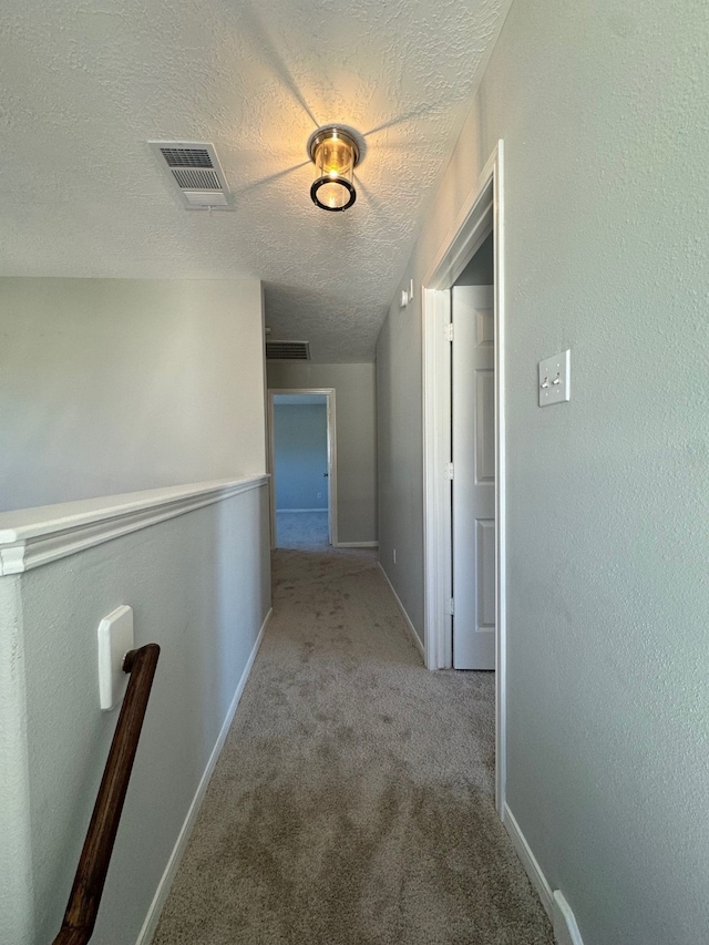 hallway with light colored carpet and a textured ceiling