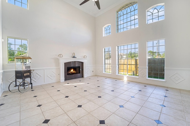 unfurnished living room with a fireplace, a towering ceiling, ceiling fan, and ornamental molding