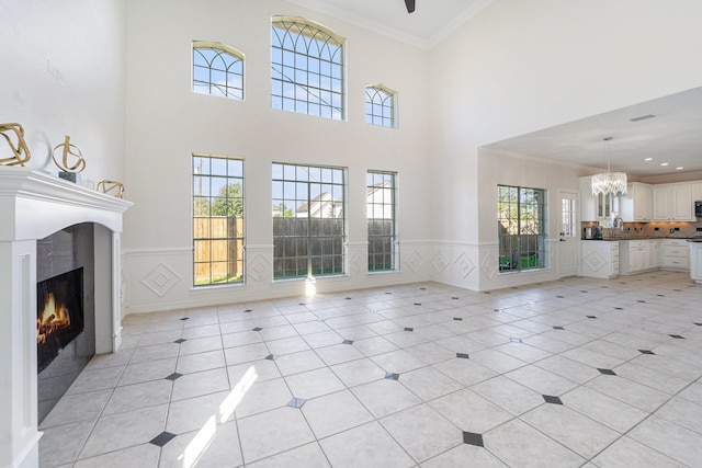 unfurnished living room featuring crown molding, sink, light tile patterned flooring, and a high ceiling