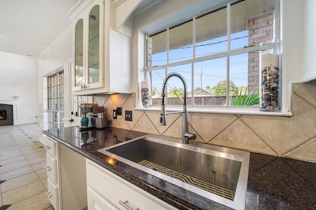 kitchen with backsplash, white cabinets, sink, ornamental molding, and a tiled fireplace