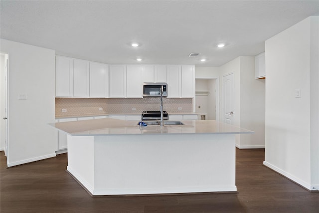 676 Imperial Loop, Alvin, TX 77511 - kitchen featuring visible vents, stainless steel microwave, a sink, an island with sink, and dark wood-style floors
