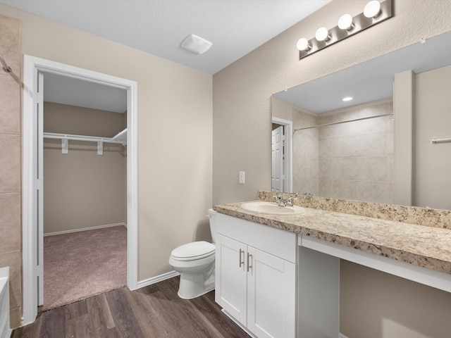 bathroom with a tile shower, hardwood / wood-style floors, vanity, and toilet