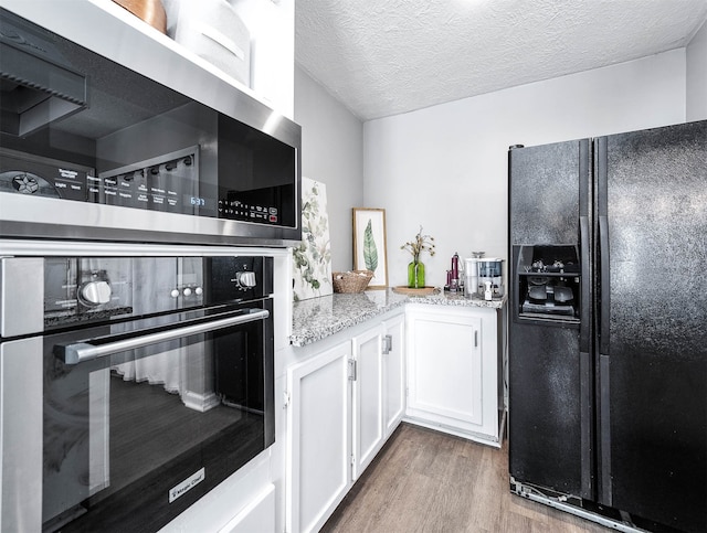 kitchen with black appliances, wood-type flooring, light stone countertops, a textured ceiling, and white cabinetry