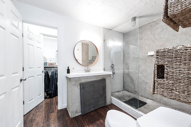 bathroom featuring vanity, toilet, a textured ceiling, a tile shower, and wood-type flooring