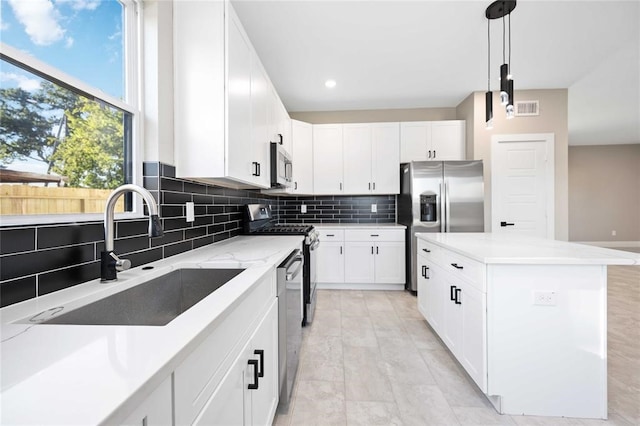 kitchen with light stone countertops, stainless steel appliances, sink, a center island, and white cabinetry