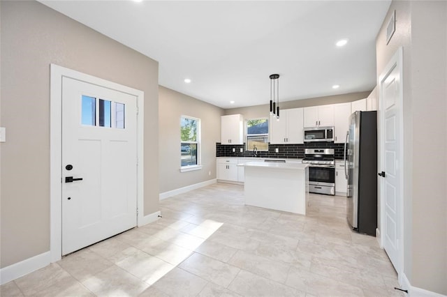 kitchen with a kitchen island, decorative light fixtures, decorative backsplash, white cabinets, and appliances with stainless steel finishes