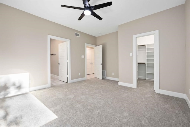 unfurnished bedroom featuring a walk in closet, ceiling fan, a closet, and light colored carpet