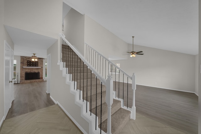 staircase featuring high vaulted ceiling, a brick fireplace, ceiling fan, and hardwood / wood-style flooring