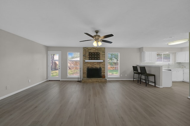 unfurnished living room with ceiling fan, wood-type flooring, and a brick fireplace